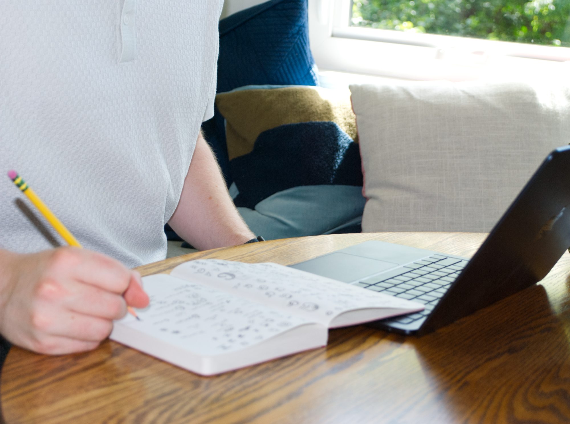 Ezrah sketching in a notebook next to his laptop