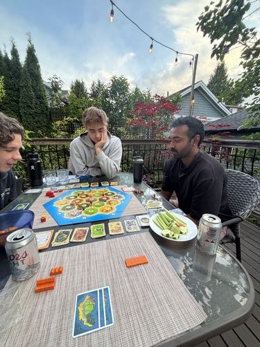 Ezrah and friends playing Catan on a patio in the evening